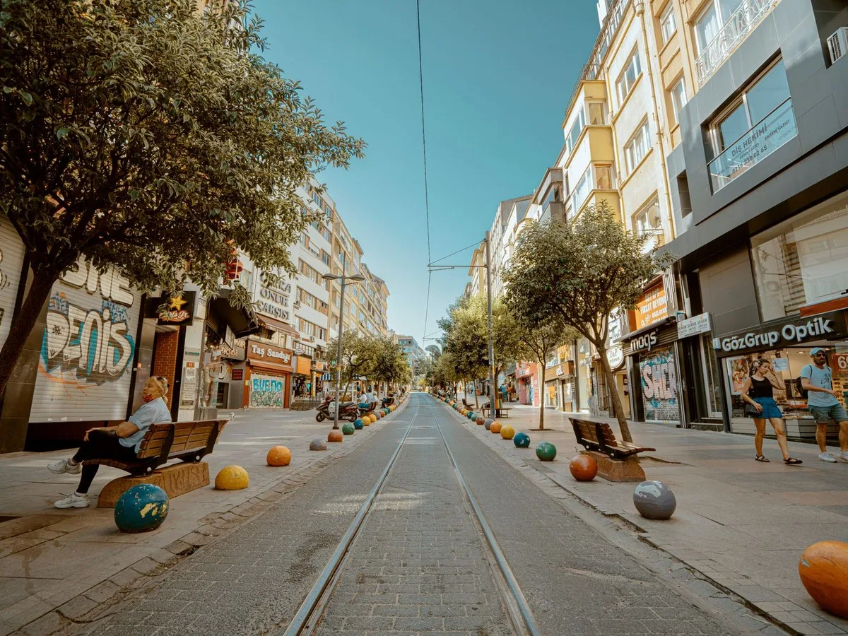 Strada con negozi, alberi e spazio per camminare.