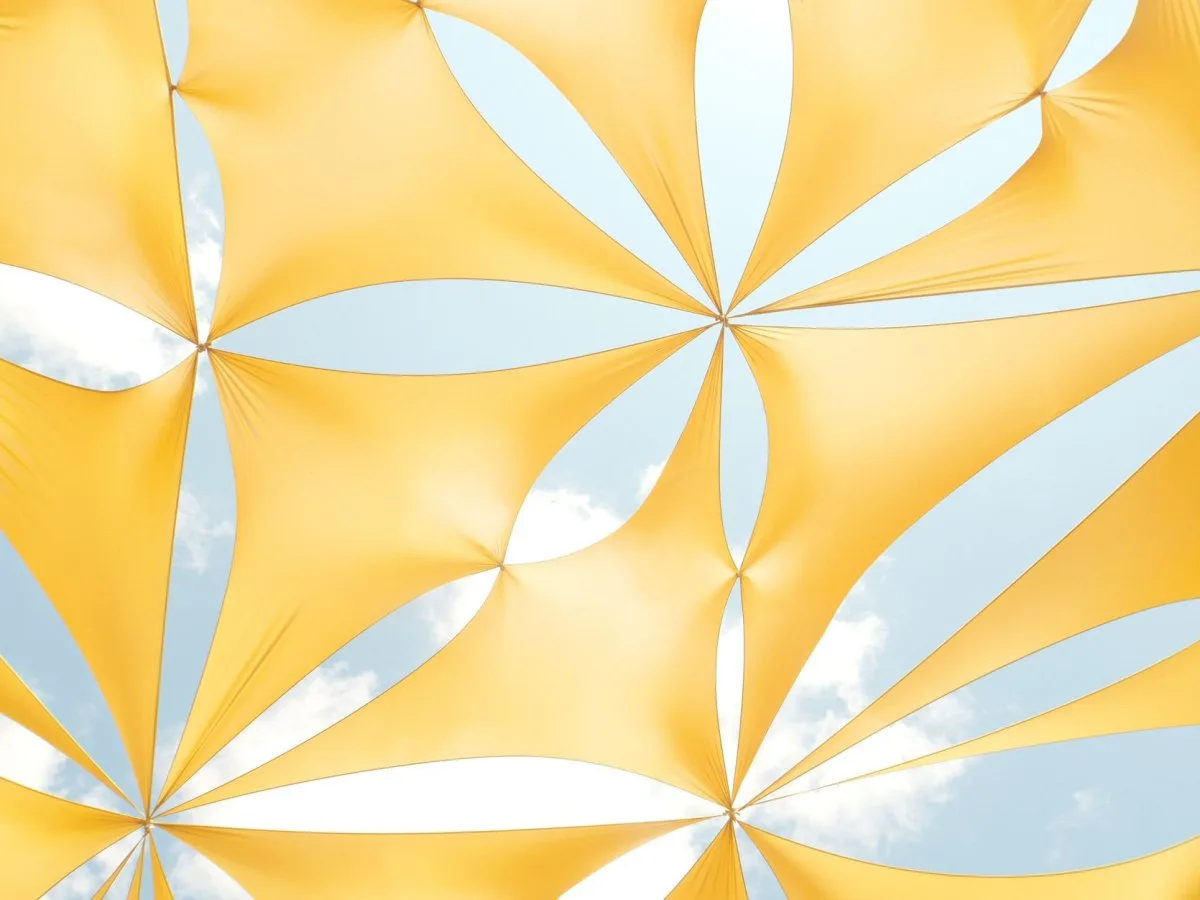 A taut yellow fabric canopy arranged in geometric panels, with openings revealing the blue sky.