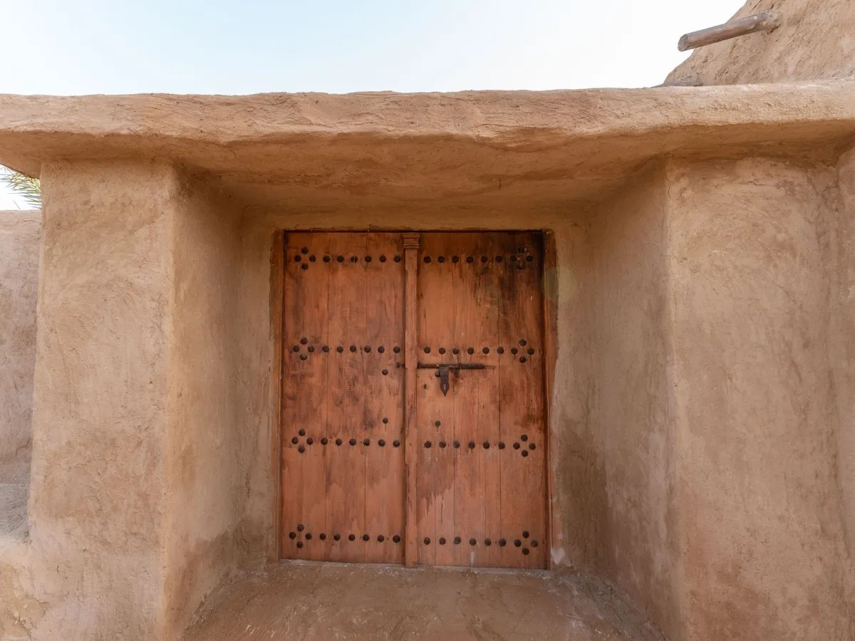Adobe facade with a double-leaf wooden door featuring studs, showing the texture of earthen architecture.