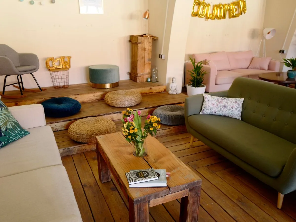 Open living room with green and pink sofas, cushions, and a wooden table with flowers, creating a cozy and personal atmosphere.